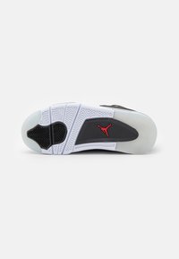 La suola di una scarpa atletica nera presenta una sezione in gomma nera texture, un intersuola bianca e una suola traslucida in gomma con motivo a spina di pesce. Dettaglio del logo rosso.