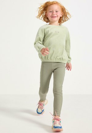 Lys grøn fleece sweatshirts med elastisk talje; parret med ribbede grønne leggings og farverige sneakers med lyserøde snørebånd.
