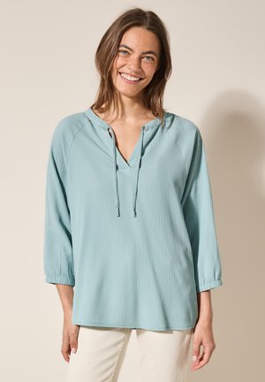 Top azzurro chiaro, con texture, dotato di scollatura a V e dettagli con lacci. Presenta maniche a tre quarti, vestibilità comoda e tessuto morbido.