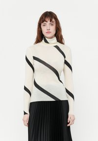 Maglione a collo alto in crema con strisce diagonali nere. Realizzato in un tessuto leggero, presenta maniche lunghe e un design aderente.