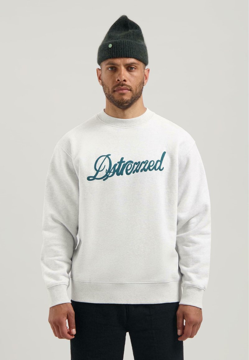 Felpa grigia chiaro con colletto a girocollo, scritta ricamata blu, polsini e orlo a coste. I pantaloni neri e un berretto verde scuro completano l'outfit.