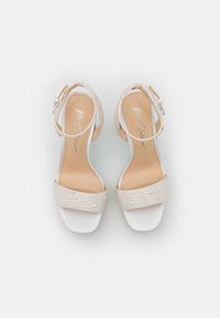 Sandali con tacco alto beige con una fascia larga decorata con strass, cinturino alla caviglia regolabile e una soletta liscia e bianca.