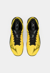 Baskets de sport jaunes avec une surface texturée, présentant des accents noirs, de lacets épais et un design épuré et profilé.