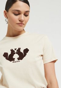 Béžové bavlnené tričko s tmavo hnedou grafikou dvoch veveričiek čelom k sebe srdcovým symbolom, pod textom "Ottod'Ame."