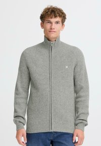 Pelēks rāvējslēdzēja džemperis ar ribotu faktūru, augstu apkakli un mazu logo uz krūtīm. Garas piedurknes un taisna piegriezuma.