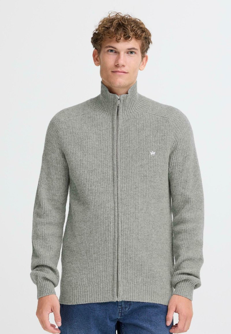 Pelēks rāvējslēdzēja džemperis ar ribotu faktūru, augstu apkakli un mazu logo uz krūtīm. Garas piedurknes un taisna piegriezuma.