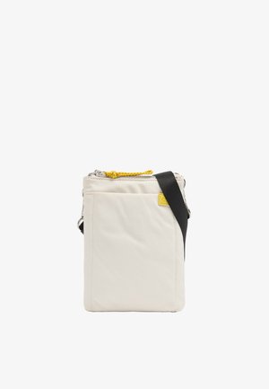 Kompaktowa kremowa torba na ramię z czarnym regulowanym paskiem, przednią kieszenią i żółtym suwakiem.