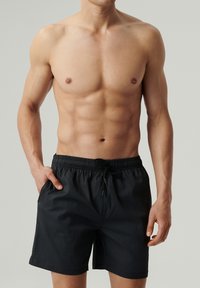 Czarne szorty kąpielowe z teksturowanej tkaniny, z elastycznym pasem i sznurkiem do regulacji. Posiadają boczne kieszenie i luźny krój.