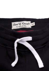 Sorte bomulds sweatpants med ribbet talje, hvid snor og en rød inderside. Har et stofmærke med mærkens navn og detaljer.