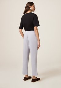 Zwart shirt met korte mouwen en ronde hals, gecombineerd met lichtgrijze tapered broek met splitten aan de onderkant, gedragen met bruine slippers.