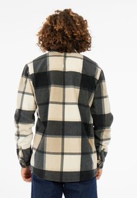 Zwarte en beige geruite flanellen shirt met lange mouwen, knoopmanchetten en een licht gebogen zoom. Zachte textuur met grote vierkante patronen.