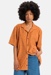 Short-sleeve, orange shirt with textured pattern. Features a collar and single chest pocket. Buttons down the front, relaxed fit.