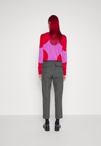 Wielokolorowy sweter z czerwonymi i różowymi okrągłymi wzorami, zestawiony z szarymi spodniami o tapered fit, posiadającymi tylne kieszenie, oraz czarnym obuwiem.