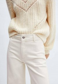 Jean taille haute beige avec une coupe slim, fabriqué en coton. Il dispose d'une fermeture à bouton métallique et d'un subtil détail de couture le long des coutures.