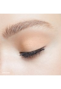 Matte eyeshadow in sandy beige tones, applied to a closed eyelid; fine eyelashes and defined eyebrow visible, smooth skin texture.