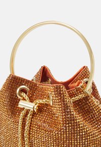 Metallisk orange dragstring bucket-väska prydd med guldfärgad hårdvara och rhinestenar, med ett runt topphandtag och en texturerad yta.