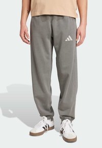 Grå sweatpants med elastisk talje, med et hvidt Adidas-logo. Lavet af blødt materiale med en afslappet pasform og ribbede manchetter.