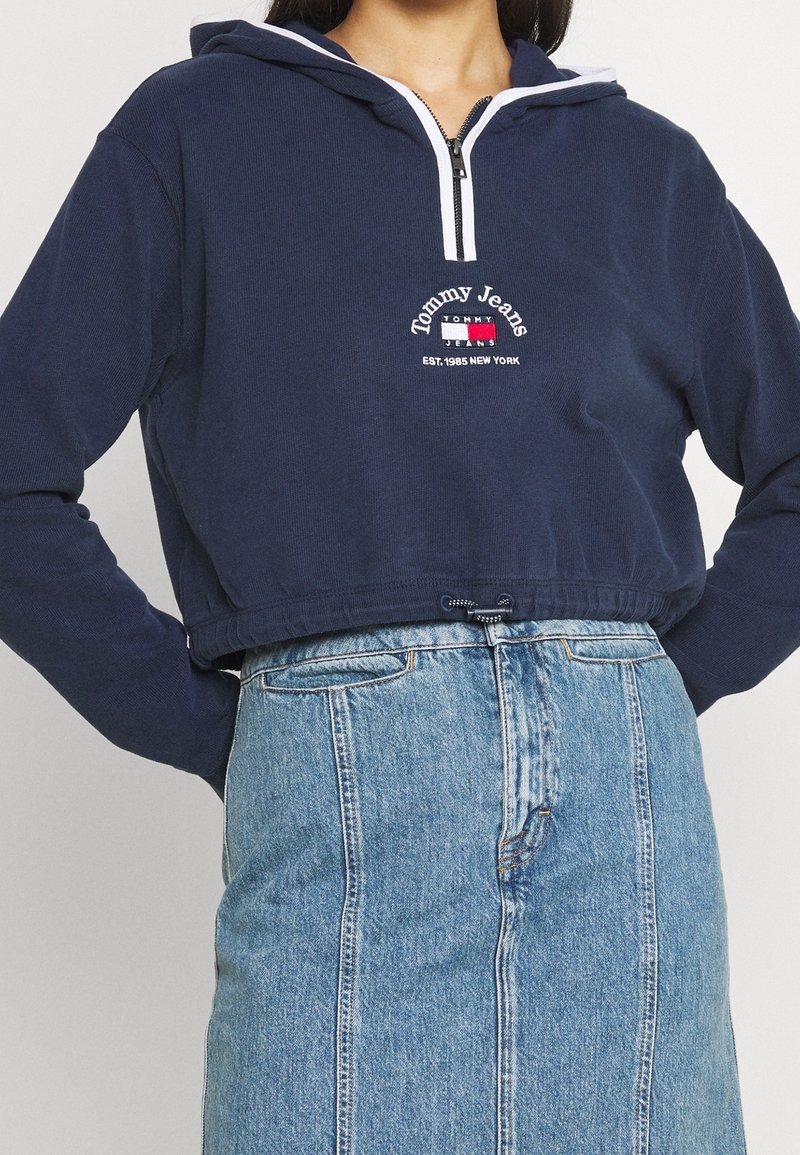 Sweat à capuche court bleu marine avec demi-fermeture éclair et logo "Tommy Jeans", associé à une jupe en jean bleue taille haute.