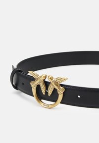 Schwarzer Leder-Gürtel mit einer goldfarbenen Metallschnalle, die wie zwei Vögel geformt ist. Das Design beinhaltet gravierte Details auf den Vögeln.
