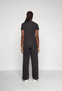 Black short-sleeve t-shirt and loose-fitting trousers. Soft fabric with a relaxed fit. Person shown from the back, wearing white shoes.