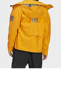 Gelbe wasserdichte Jacke mit Kapuze, ausgestattet mit einem Rückenbelüftung, grauer Innenausstattung und drei vertikalen Streifen in Lila und Blau auf dem Rücken.