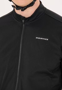 Veste de cyclisme noire avec un tissu texturé, fermeture éclair intégrale et logo réfléchissant "ENDURANCE" sur le devant.