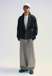 Black wool-blend oversized double-breasted jacket, white crew neck t-shirt, grey wide-leg trousers, and black platform shoes. Relaxed fit.