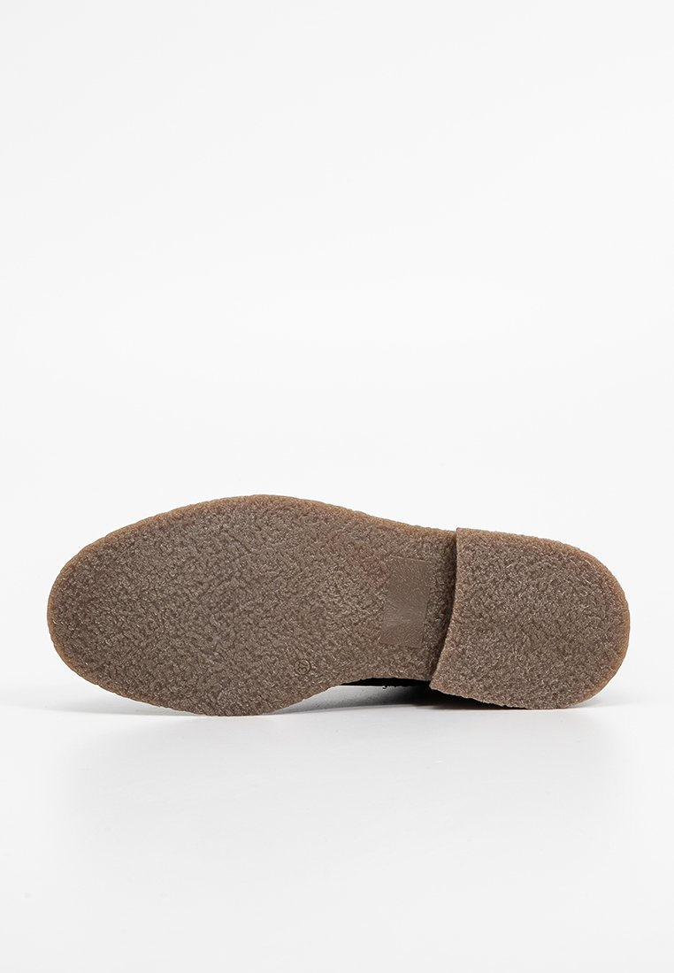 Sohle eines Schuhs mit einer strukturierten, braunen Gummioberfläche; abgerundete Form mit einem leichten Absatz und einem flachen Zehenbereich. Keine sichtbaren Muster.