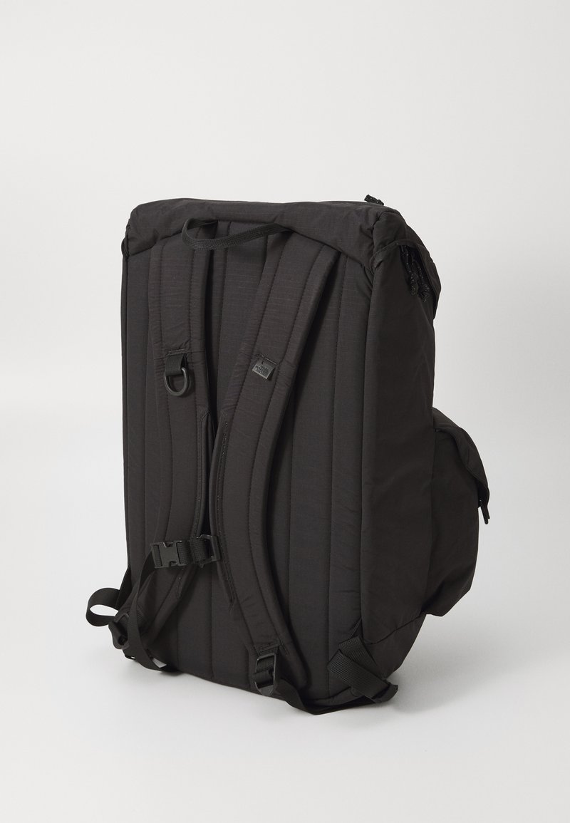 Sac à dos noir en tissu rembourré, avec des bretelles ajustables, une poche latérale et une poignée supérieure. Il présente un design minimaliste et des fermetures éclair.