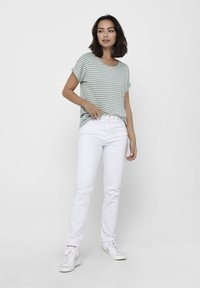 T-shirt à rayures vertes et blanches à manches courtes associé à un jean blanc, doté d'une coupe décontractée et d'un col rond. Des baskets blanches viennent compléter le look.