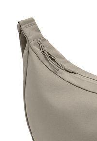 Beige szövet válltáska texturált felülettel, ívelt formával és cipzárral, amelyen hurkos húzók vannak a könnyű hozzáférés érdekében.