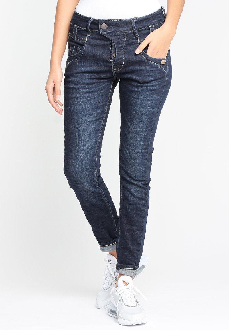 Smala mörkblå jeans med en slät textur, fem fickor och lätt blekning. Har en knappstängning och sydda detaljer.