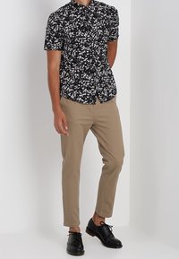 Lyhythihainen musta paita, jossa valkoinen kukkakuvio, yhdistetty vaaleanruskeisiin slim-fit-housuihin ja mustiin nyörikenkiin. Yksinkertainen napillinen malli.