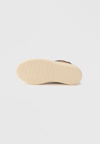 Pantof de culoare maro cu un superior texturat și o talpă din cauciuc cu un model bej. Prezintă branding și un design plat, potrivit pentru ținute casual.