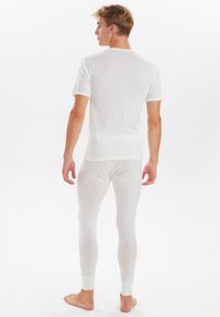 Hvid tætsiddende termisk top med korte ærmer og matchende lange bukser, lavet af et blødt, let materiale, med minimale sømme og ribbede manchetter.