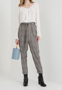 Blusa bianca a volant, pantaloni grigi a quadri con cintura, stivali neri alla caviglia e una borsa rotonda blu con manico giallo.