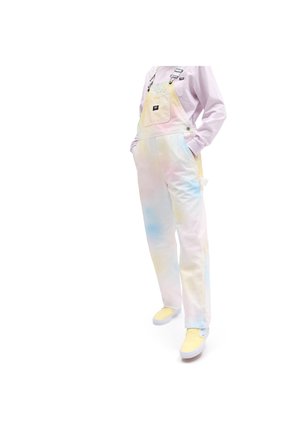 Pastel tie-dye tuinbroek in roze, blauw en geel met verstelbare bandjes, een voorzak en een relaxte pasvorm. Gecombineerd met gele instappers.