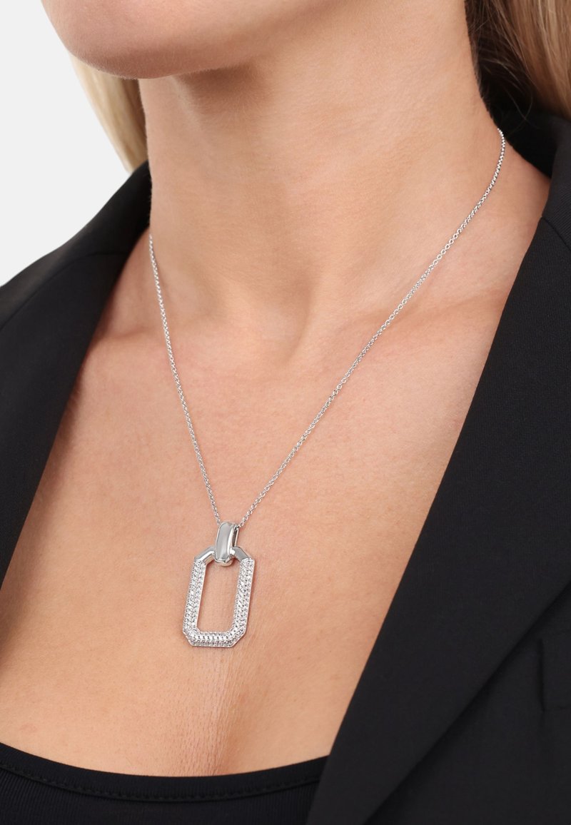 Collar de plata con un colgante rectangular que presenta un borde texturizado y piedras de strass transparentes, suspendido de una delicada cadena.