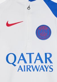 Maillot de sport blanc avec des accents bleus, arborant un swoosh rouge de Nike, un logo circulaire du Paris Saint-Germain, et "QATAR AIRWAYS" en texte bleu.