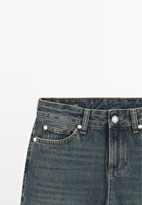 Jeans in denim blu scuro con vita alta, design con cinque tasche, accessori in argento e cuciture a contrasto. Include passante per cintura e etichetta del marchio.