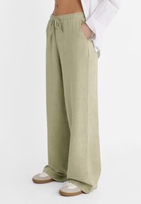 Lichtgroene wijde broek van een zachte, gestructureerde stof met een elastische tailleband en een koord. Gepaard met beige sneakers.