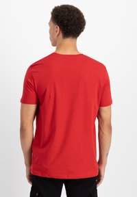 Červené bavlněné tričko s krátkými rukávy a kulatým výstřihem. Zadní strana má hladkou texturu a jednoduchý, klasický design.