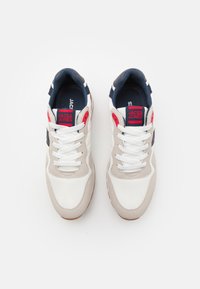 Weiße und graue Sportschuhe mit marineblauen Akzenten, aus Mesh- und Wildledermaterialien, flachen Schnürsenkeln und einer Gummisohle. Markenlogo auf der Zunge sichtbar.