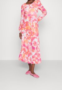 Robe à manches longues tie-dye dans des tons de rose et d'orange, avec une jupe à volants et un col rond, assortie à des chaussures plates rose pâle.