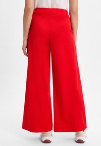 Rode wijde broek met een elastische tailleband en een gladde textuur, met een rechte zoom en gecombineerd met lichtgekleurde sneakers.