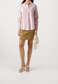 Lys pink langærmet skjorte med knapper, tætsiddende khaki mini-nederdel med sideslids, beige hælede sandaler og en hvid håndtaske.