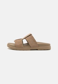 Sandales en cuir suédé marron avec une tige douce, une sangle ajustable, une semelle intérieure rembourrée et une semelle extérieure en caoutchouc texturé pour une meilleure adhérence. Design minimaliste.