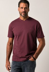 Camiseta de manga corta en color burdeos con escote en V, fabricada en una tela suave, que presenta un sutil logo en el pecho y se combina con jeans de mezclilla oscura.