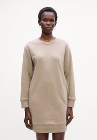 Beige Sweatshirtkleid aus weichigem Material, mit langen Ärmeln, Rundhalsausschnitt und gerippten Bündchen sowie einem kleinen gestickten Logo auf der Brust.