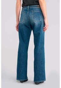 Jeans de mezclilla azul acampanados que presentan un canesú trasero, dos bolsillos traseros con costuras en contraste y una cintura de altura media.